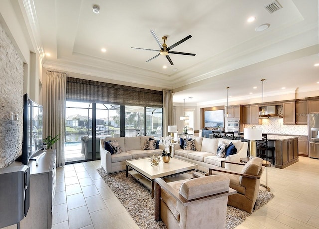 living area featuring a ceiling fan, a raised ceiling, visible vents, and crown molding