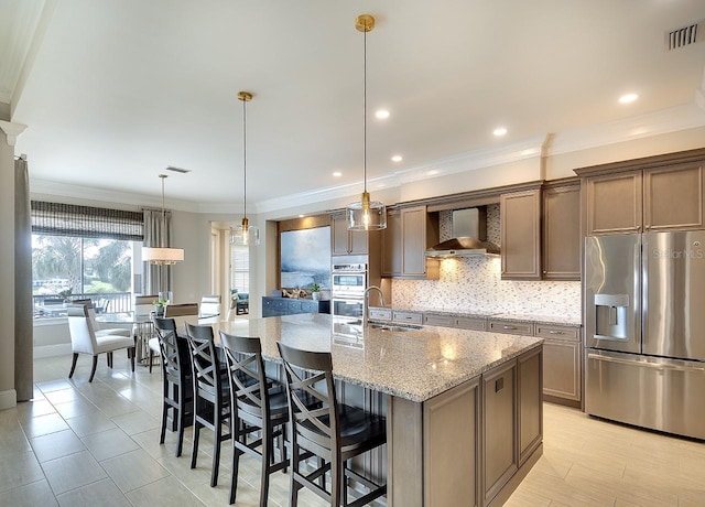 kitchen featuring tasteful backsplash, visible vents, stainless steel appliances, wall chimney range hood, and a sink