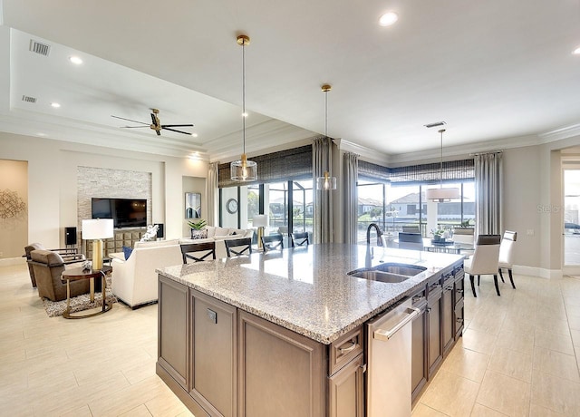 kitchen with crown molding, visible vents, a sink, an island with sink, and light stone countertops