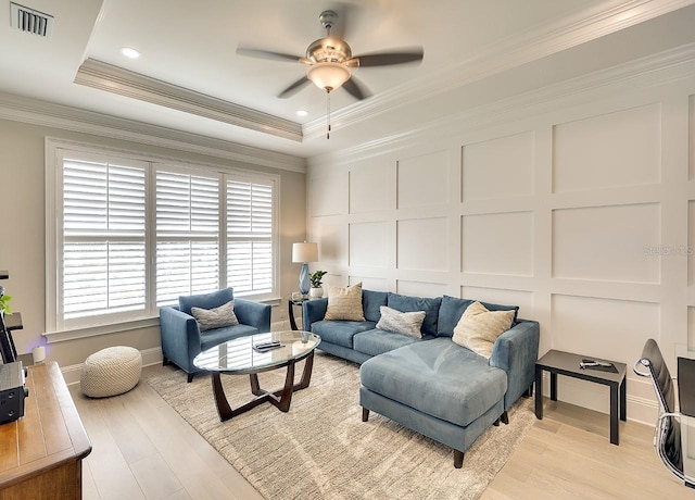 living area with crown molding, light wood finished floors, a raised ceiling, visible vents, and a decorative wall