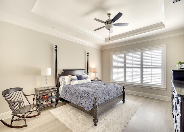 bedroom featuring light wood finished floors, visible vents, baseboards, ornamental molding, and a tray ceiling