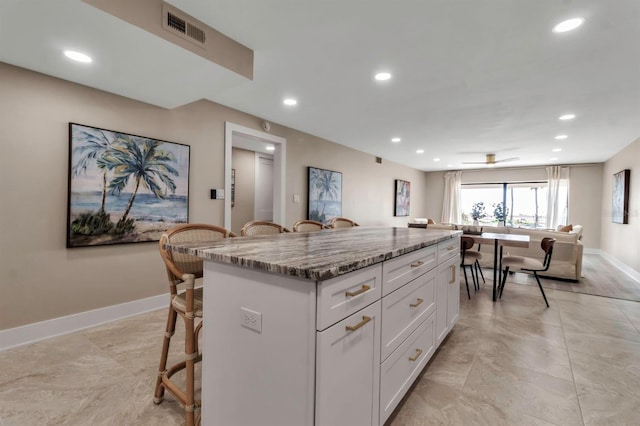 kitchen with visible vents, baseboards, a kitchen island, a kitchen breakfast bar, and white cabinetry