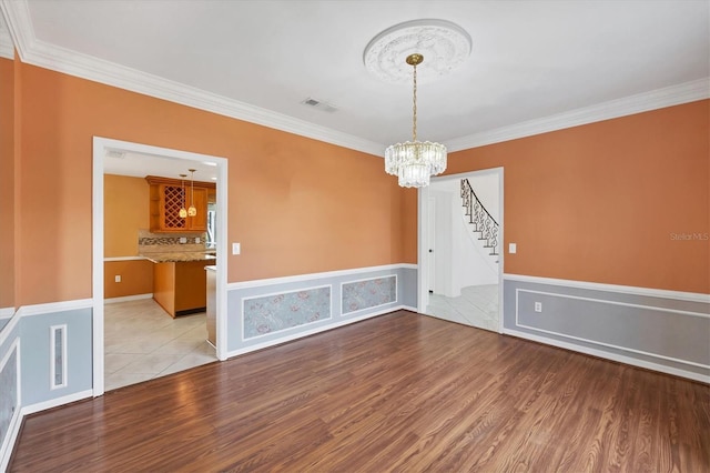 empty room featuring visible vents, stairway, wood finished floors, an inviting chandelier, and crown molding