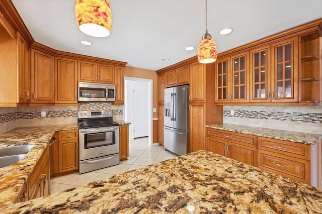 kitchen with light tile patterned floors, stainless steel appliances, brown cabinets, light stone countertops, and decorative light fixtures