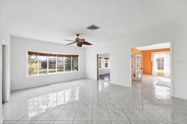 spare room featuring a textured ceiling, light tile patterned flooring, visible vents, and a ceiling fan