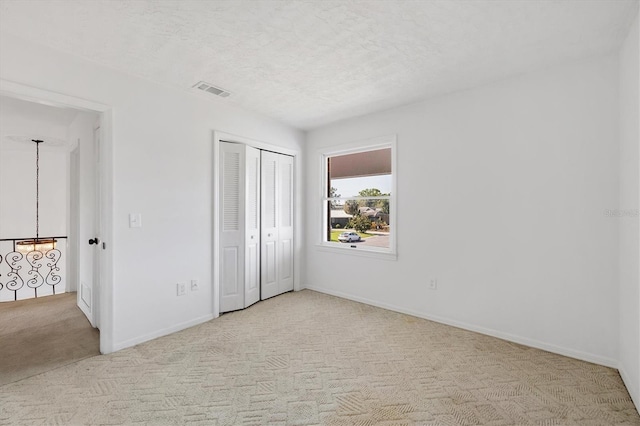 unfurnished bedroom with a textured ceiling, carpet floors, visible vents, baseboards, and a closet