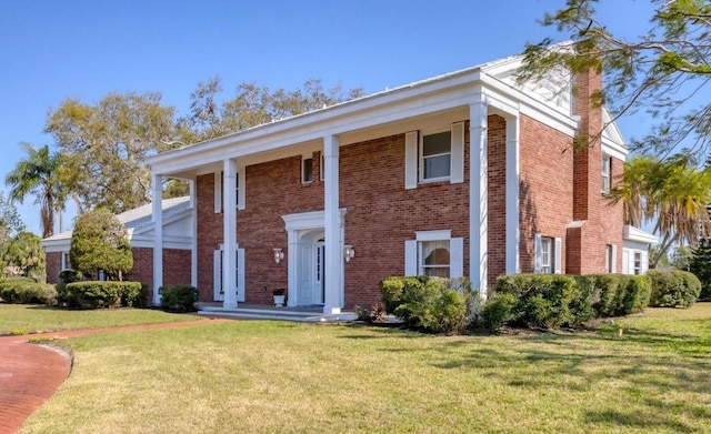 greek revival house featuring brick siding, a chimney, and a front lawn