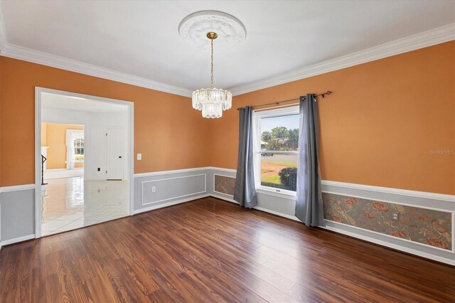 spare room featuring ornamental molding, wood finished floors, a notable chandelier, and a wainscoted wall