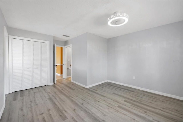 unfurnished bedroom with baseboards, a closet, wood finished floors, and visible vents