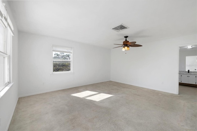 empty room with baseboards, ceiling fan, light carpet, and visible vents