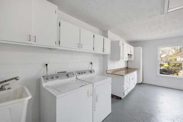 laundry area featuring a sink, a textured ceiling, washing machine and dryer, and cabinet space