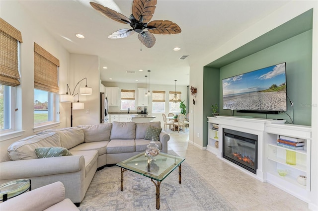 living room with baseboards, a healthy amount of sunlight, a glass covered fireplace, and recessed lighting