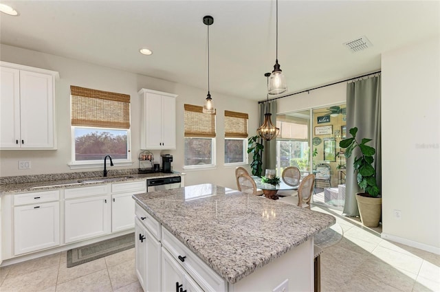 kitchen featuring stainless steel dishwasher, white cabinetry, a kitchen island, a sink, and light stone countertops