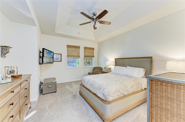 bedroom featuring a raised ceiling, light colored carpet, ceiling fan, and baseboards