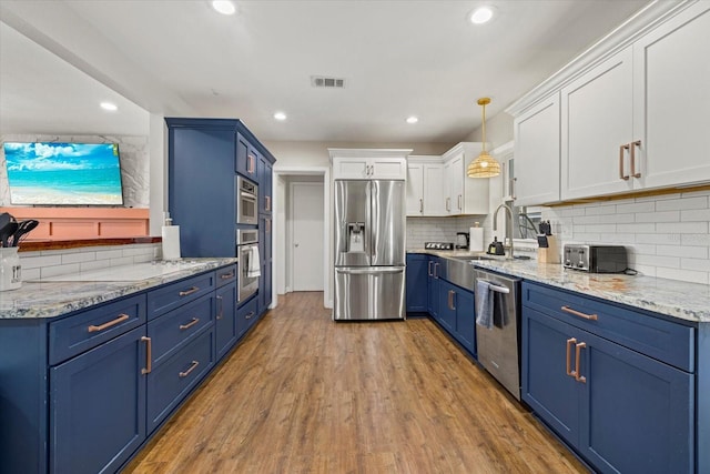 kitchen featuring stainless steel appliances, wood finished floors, a sink, visible vents, and blue cabinetry