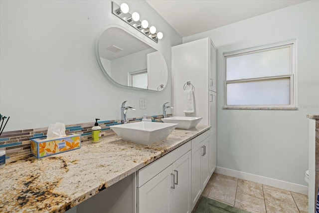 bathroom with tasteful backsplash, a sink, baseboards, and double vanity