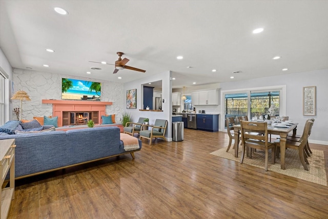 living area with ceiling fan, a glass covered fireplace, wood finished floors, and recessed lighting