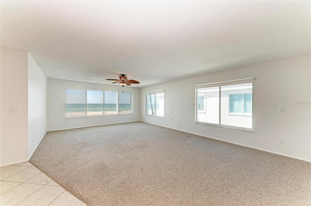 spare room featuring ceiling fan, light tile patterned flooring, baseboards, and light colored carpet