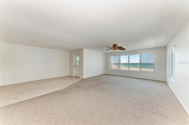 spare room featuring a textured ceiling, ceiling fan, light tile patterned flooring, and light colored carpet