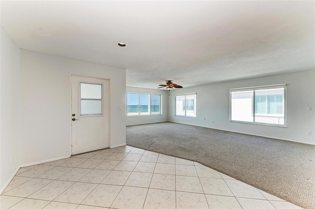 spare room with light carpet, light tile patterned floors, ceiling fan, and baseboards