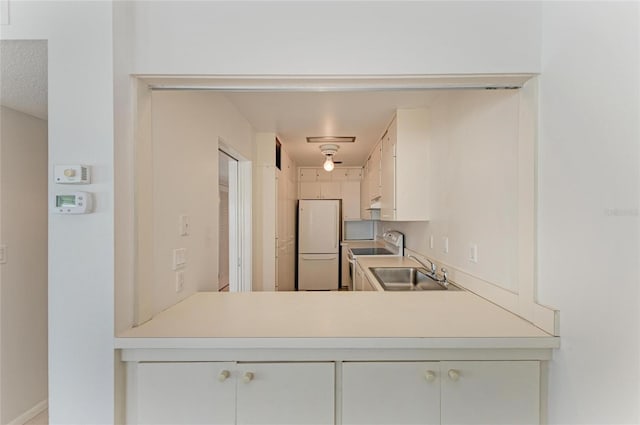 kitchen featuring electric range oven, freestanding refrigerator, range hood, light countertops, and a sink