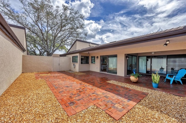 rear view of property featuring a gate, stucco siding, a patio, and fence