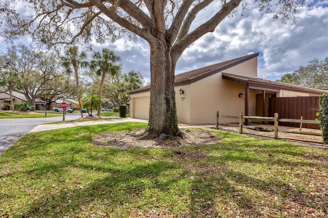 view of side of home featuring a yard, stucco siding, an attached garage, fence, and driveway