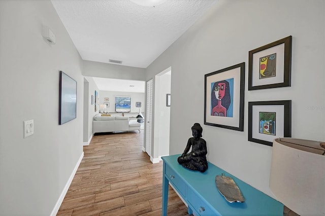 hallway featuring a textured ceiling, wood finish floors, visible vents, and baseboards