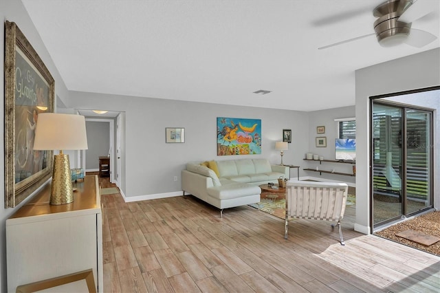 living room with light wood finished floors, a ceiling fan, visible vents, and baseboards