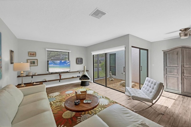 living area with ceiling fan, a textured ceiling, visible vents, and light wood-style floors