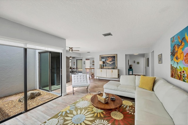 living area with a ceiling fan, visible vents, a textured ceiling, and wood finished floors