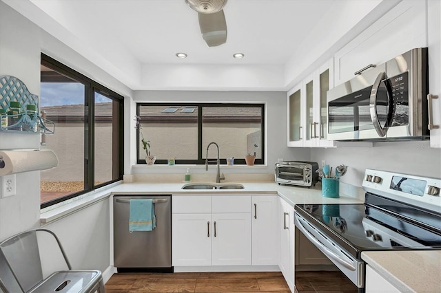 kitchen with stainless steel appliances, light countertops, glass insert cabinets, white cabinetry, and a sink