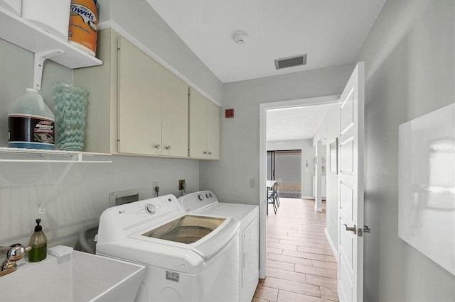 laundry room with cabinet space, visible vents, washing machine and clothes dryer, wood finish floors, and a sink