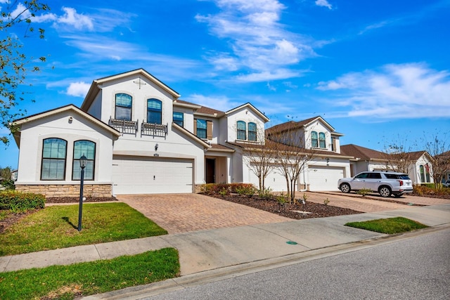 view of front of home featuring an attached garage, stone siding, decorative driveway, and stucco siding