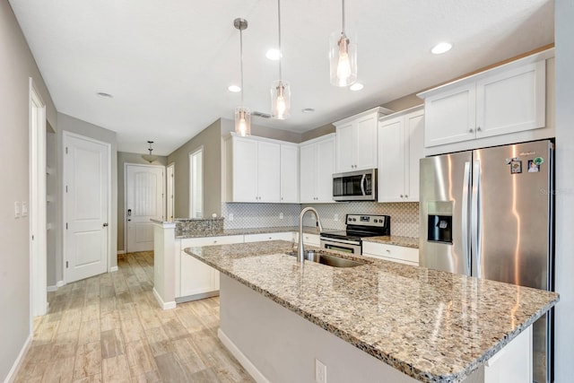 kitchen featuring stainless steel appliances, white cabinets, an island with sink, and decorative backsplash