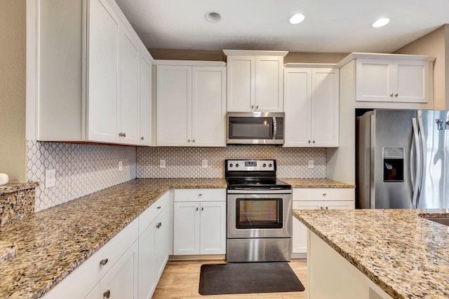 kitchen featuring stainless steel appliances, white cabinets, light stone counters, and decorative backsplash