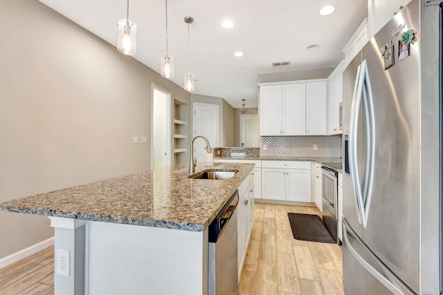 kitchen with a center island with sink, light wood finished floors, stainless steel appliances, backsplash, and a sink