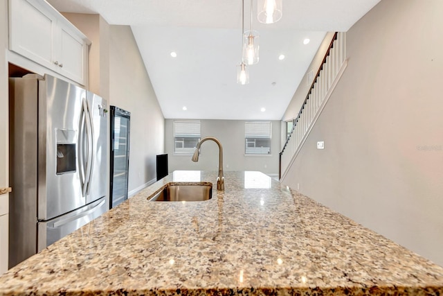 kitchen with a kitchen island with sink, a sink, white cabinets, stainless steel refrigerator with ice dispenser, and light stone countertops