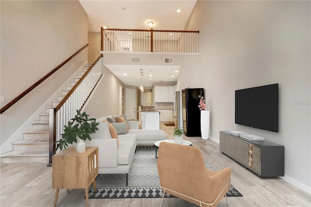 living area featuring visible vents, a towering ceiling, stairs, baseboards, and light wood-type flooring