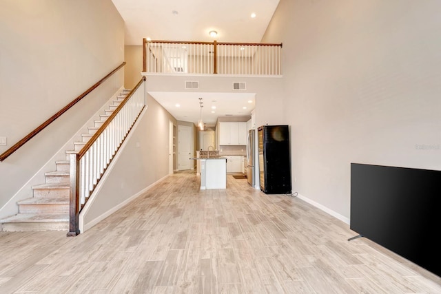 unfurnished living room with light wood-style floors, visible vents, baseboards, and stairs