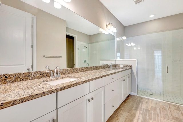 full bathroom with double vanity, wood finished floors, a sink, and a shower stall