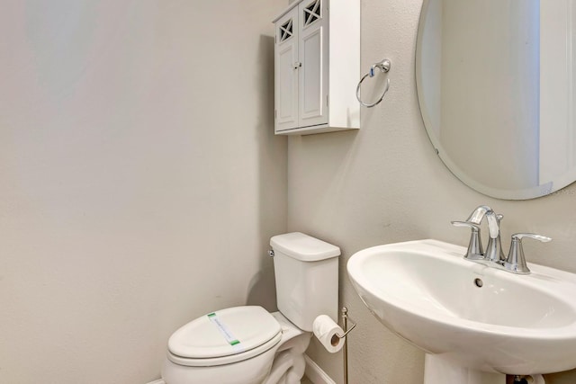 half bathroom featuring toilet, baseboards, and a sink