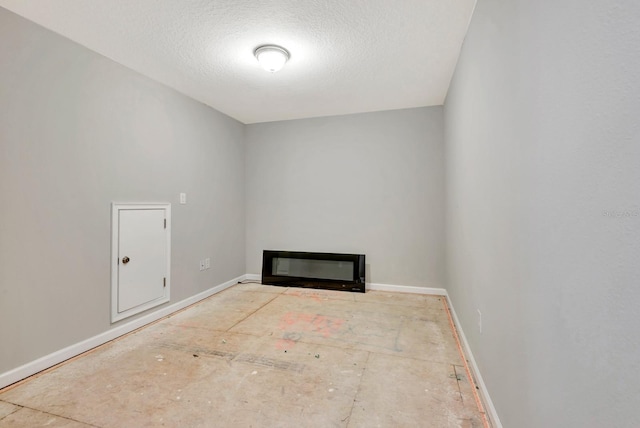 empty room with baseboards, a textured ceiling, and a glass covered fireplace