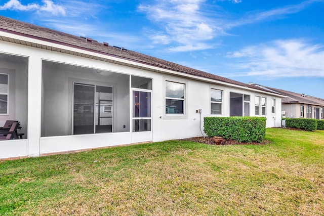 rear view of house with a sunroom, stucco siding, and a yard