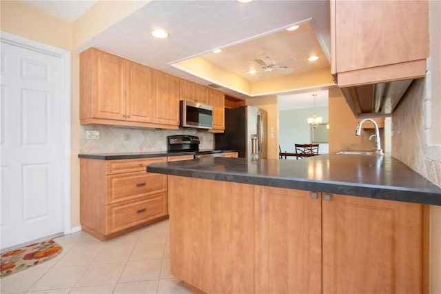 kitchen featuring dark countertops, appliances with stainless steel finishes, a peninsula, a tray ceiling, and a sink