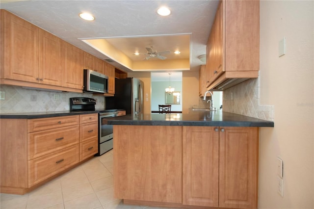 kitchen featuring dark countertops, a raised ceiling, appliances with stainless steel finishes, a sink, and a peninsula