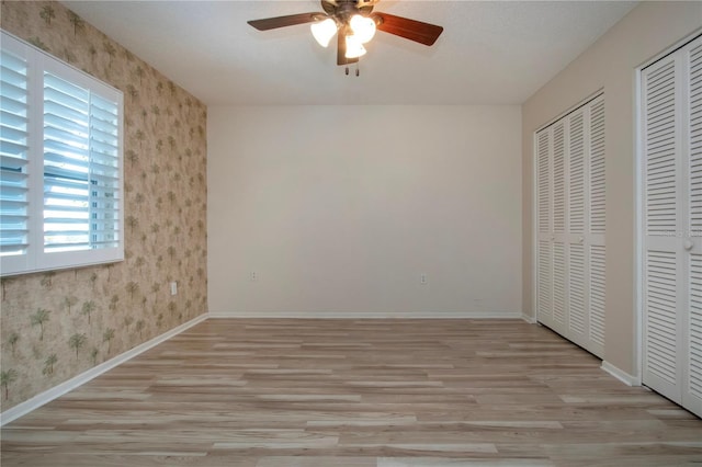 unfurnished bedroom featuring ceiling fan, baseboards, multiple closets, light wood-type flooring, and wallpapered walls