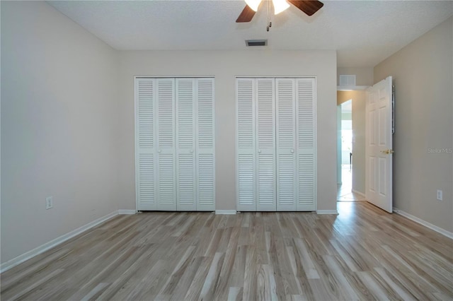 unfurnished bedroom featuring a textured ceiling, light wood-style flooring, visible vents, baseboards, and two closets