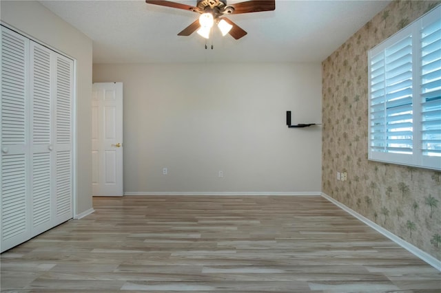 unfurnished bedroom featuring a closet, light wood-style flooring, a ceiling fan, baseboards, and wallpapered walls