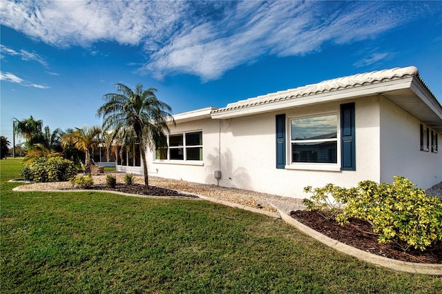 view of side of property featuring a tile roof, a yard, and stucco siding